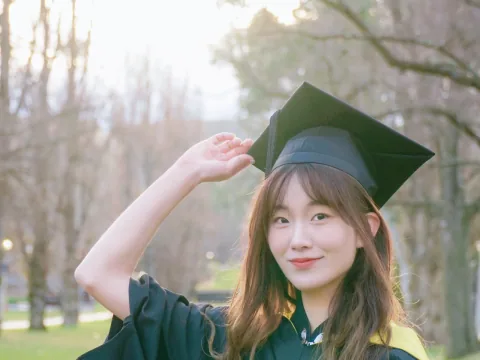 A graduate smiling outdoors in cap and gown